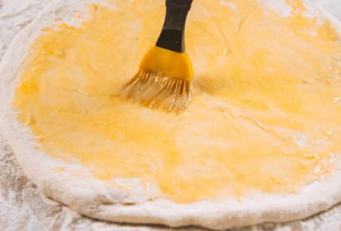 Pizza hamuru, aşçı mutfakta yumurta sarısı ve pasta fırçası sürüyor.