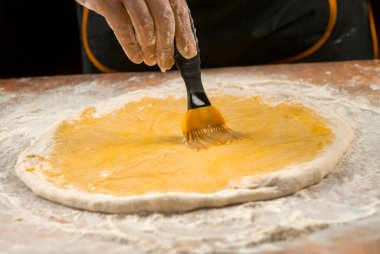 Pizza hamuru, aşçı mutfakta yumurta sarısı ve pasta fırçası sürüyor.