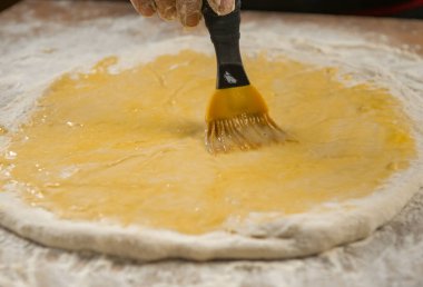 Pizza hamuru, aşçı mutfakta yumurta sarısı ve pasta fırçası sürüyor.