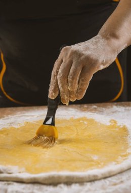 Pizza hamuru, aşçı mutfakta yumurta sarısı ve pasta fırçası sürüyor.