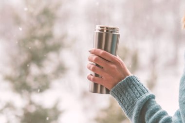 Kadın bir termos şişe elinde bir kış ormanda arka planda