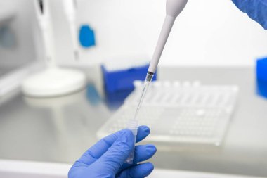 Bir laboratuvar teknisyeninin ellerinde bir tüp kan örneği ve diğer numunelerle dolu bir raf var. Üzerinde çalışmak için kan tüpü örneği tutan laboratuvar teknisyeni. Corona virüsü salgını konsepti. Coronavirus aşısı gelişimi.