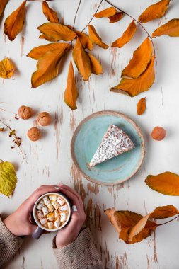 Pasta, ceviz ve saçılmış yapraklarla, sonbahar kompozisyonu eşliğinde eski püskü bir masada lokum tutan kadınların üst görüntüsü.