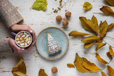 Pasta, ceviz ve saçılmış yapraklarla, sonbahar kompozisyonu eşliğinde eski püskü bir masada lokum tutan kadınların üst görüntüsü.