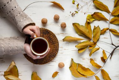 Eski ahşap masanın üzerinde kurumuş yaprakları olan bir fincan çay tutan kadın elleri. Sonbahar konsepti. Yaklaş, seçici odaklanma