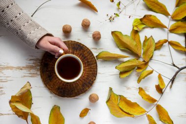 Eski ahşap masanın üzerinde kurumuş yaprakları olan bir fincan çay tutan kadın elleri. Sonbahar konsepti. Yaklaş, seçici odaklanma