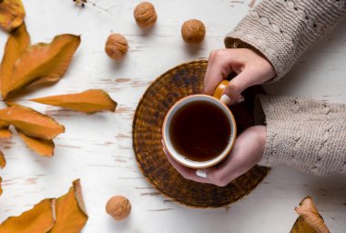 Eski ahşap masanın üzerinde kurumuş yaprakları olan bir fincan çay tutan kadın elleri. Sonbahar konsepti. Yaklaş, seçici odaklanma