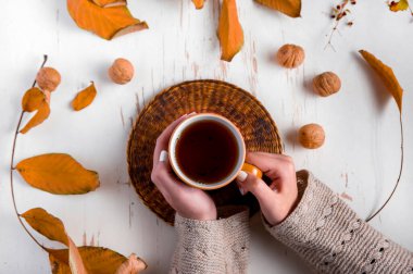 Eski ahşap masanın üzerinde kurumuş yaprakları olan bir fincan çay tutan kadın elleri. Sonbahar konsepti. Yaklaş, seçici odaklanma