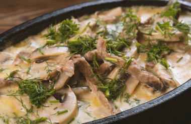 Biftek parçalarından yapılmış bir tabak, koyu ahşap üzerinde krema soslu mantar.