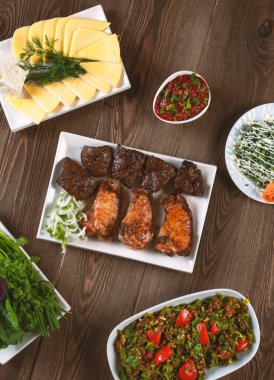 Izgara et, salata, peynir, ahşap bir masada otlar, üst manzara.