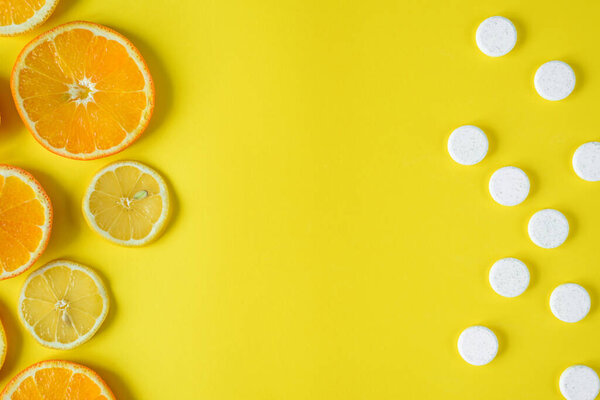 Вид сверху на фрукты и белые таблетки друг напротив друга на желтом фоне, концепция фруктов на фоне синтетических витаминов, свободное пространство для текста в середине
