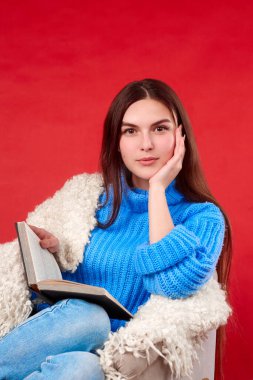  Mavi kazaklı bir kız koltukta kitap okuyor.