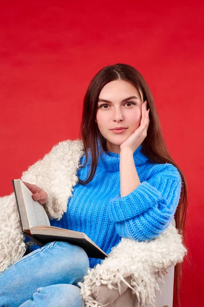 Dívka v modrém svetru čte knihu na křesle Stock Fotografie