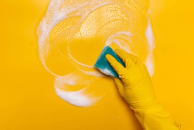  Sarı arka plandaki köpüğü mavi eldivenli süngerle sil.