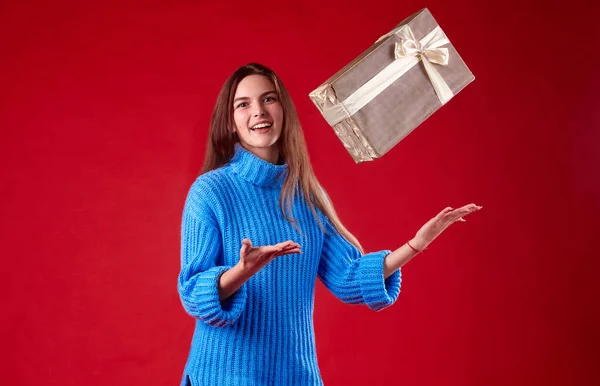 Dívka v modrém svetru chytí dárky ve vzduchu na červeném pozadí Stock Snímky