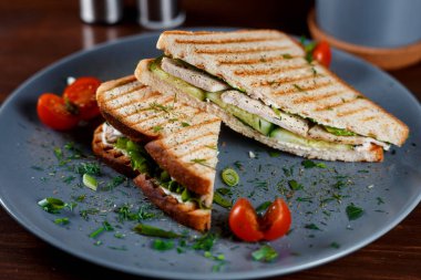 Kızarmış tavuk göğsü ve salata sandviçi. Kahverengi bir kağıda sarılmış, ahşap bir masada servis ediliyor.