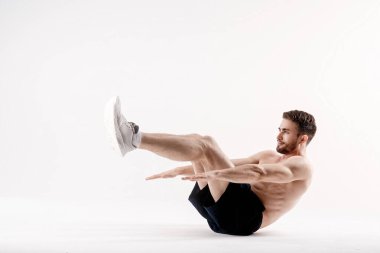 Spor fiziği olan genç bir adam, beyaz bir izole edilmiş karın boşluğunun kasları üzerinde egzersiz yapıyor.