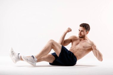Spor fiziği olan genç bir adam, beyaz bir izole edilmiş karın boşluğunun kasları üzerinde egzersiz yapıyor.