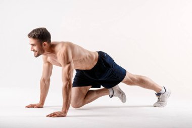 Spor fiziği olan genç bir adam, beyaz bir izole edilmiş karın boşluğunun kasları üzerinde egzersiz yapıyor.