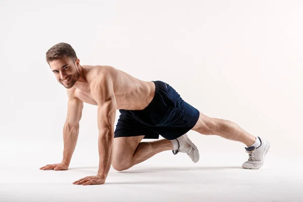 Joven con una barba de un físico deportivo hace un ejercicio sobre los músculos de la cavidad abdominal en un blanco aislado — Foto de Stock