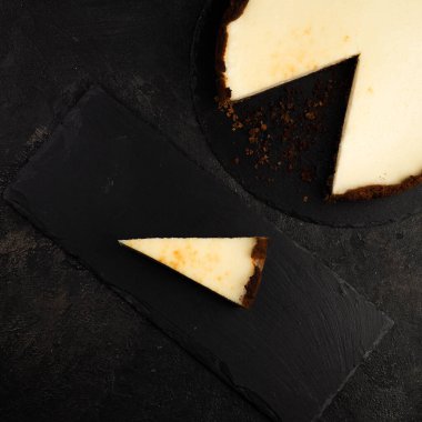 Lezzetli ev yapımı klasik New York peynirli keki ve koyu arkaplanda dilimi olan kompozisyon. Üst görünüm.