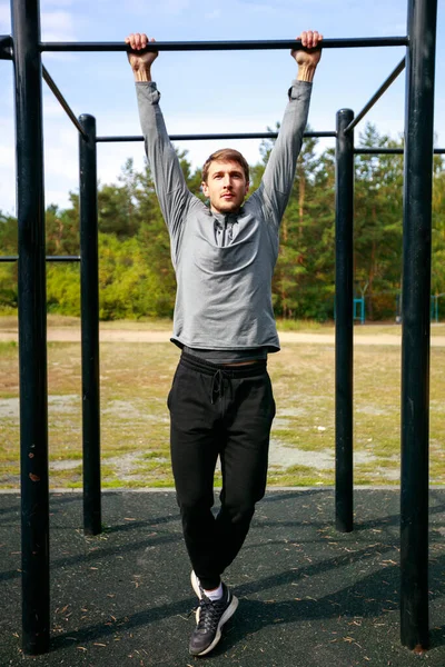 Muscular sports trainer on street workout exercising. Fit and athletic man working out in an outdoor gym. Pull ups on horizontal bar.