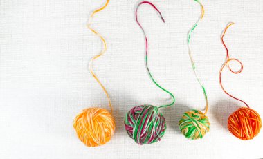 Açık desenli kumaş arkaplanda sıralanmış dört renkli iplik yumağı. Parlak turuncu, yeşil ve çok renkli iplik kopyalama alanı ile basit bir kompozisyon oluşturur. Örgü, el yapımı zanaat kavramı