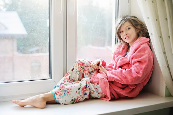 Schönes kleines Mädchen im Bademantel am Fenster — Stockfoto