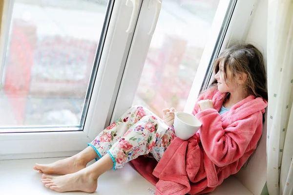 Schönes kleines Mädchen im Bademantel mit einer Tasse Tee — Stockfoto