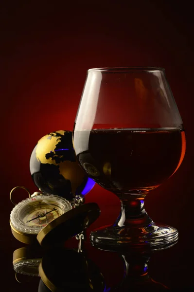 一杯带有罗盘和地球仪的科涅克威士忌 盖在深红色和黑色的背景上 — 图库照片