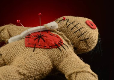 Bir vudu bebeğinin kalbinde koyu kırmızı ve siyah bir zemin üzerinde birkaç iğne sıkışır..