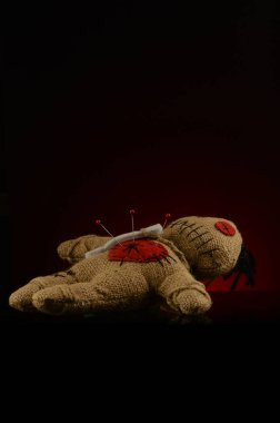 Bir vudu bebeğinin kalbinde koyu kırmızı ve siyah bir zemin üzerinde birkaç iğne sıkışır..