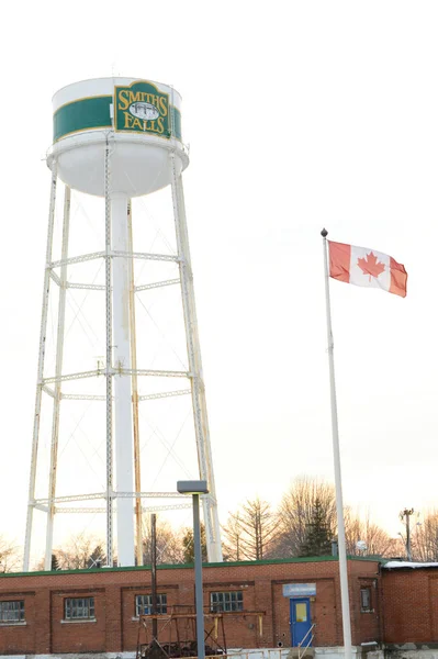 SMITHS FALls, ONTARIO, CANADA, 10 Mart 2021: Smiths Falls Watertower ve Kanada Bayrağı 'nın küçük kasabadaki Beckwith St Bridge bölgesinden bir görüntüsü.