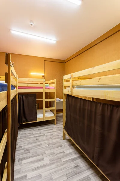 Wooden bunk beds with curtains in a large hostel dorm room