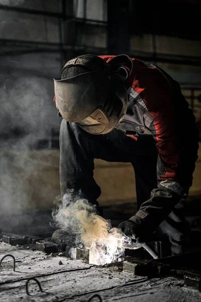 Industrial worker at a factory welding steel structure. A worker with a protective mask is welding metal using a welding machine, there is a lot of smoke around