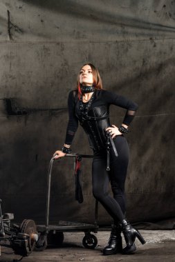 Siyah korseli ve siyah arka planda deri koşumları olan genç bir kadın. Cinsel bdsm oyuncağı. Esaretli kadın. Bdsm oyunları oynamak için giyinmiş..