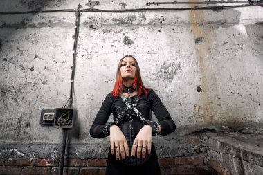 Siyah korseli, seksi baskın kadın deri kemer ve bileziklerle elleri deri bilezik ile bağlanmış, yetişkinler için oyuncaklar endüstriyel bir arka planda koyu renk görünüyor. 