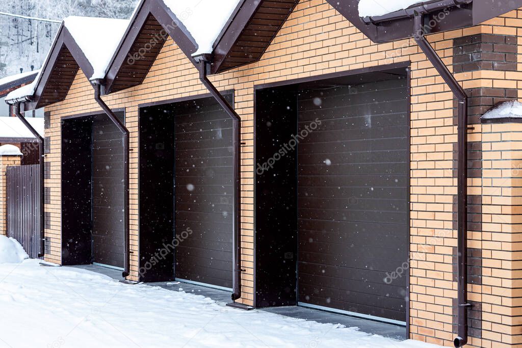 Large plan light brick garage for three cars with automatic gates in a winter village, soft focus and snowfall. Winter country life