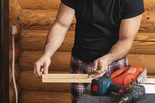 Close up of experienced carpenter in work clothes and small buiness owner  carpenter saw and processes the edges of a wooden bar with a jig saw  in a workshop