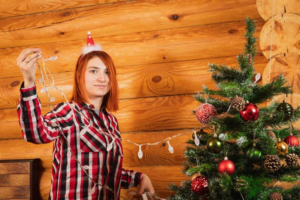 Веселая Женщина Клетчатой Рубашке Вешает Гирлянду Рождественскую Елку Фоне Зажженного — стоковое фото