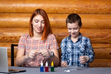 Kimya eğitimi ve eğitim konsepti. Çocuk ve annesi, bilim adamları deney tüpünden kimyasal elementlerle dolu bir kaba bir karışım döküyorlar. Deneyler için, bir kaşık, bir torba ve bir kavanoz çözelti evdeki masada.