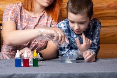 Kimya eğitimi ve eğitim konsepti. Çocuğa ve annesine yakın çekim yapan bilim adamları deney tüpünden kimyasal elementlerle dolu bir kaba bir karışım döküyorlar. Deneyler için, bir kaşık, bir torba ve bir kavanoz çözelti evdeki masada.