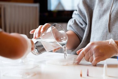 Kimya eğitimi ve eğitim konsepti. Bir çocuk ve annesinin yakın çekimlerinde, bilim adamları evde deneyler yapmak için kimyasal elementlerle dolu bir şişeye su dökerler. 