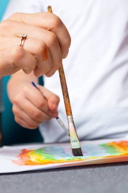 Çocukların yaratıcılığı. Anne ve çocuk, anaokulu için suluboya ev ödevlerini mavi arka plana boyuyorlar.