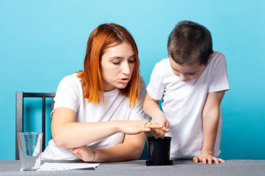 Bir anne ve oğlunun yere delikler açtığı ve tohum ekmek için toprağı gevşettiği ve mavi arka planda bir masada bitki yetiştirdiği yakın plan. Çocuklarla bahçe kursu kavramı.