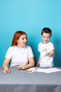 Çocukların yaratıcılığı. Anne ve oğlu mavi arka planda boya yapıyorlar.