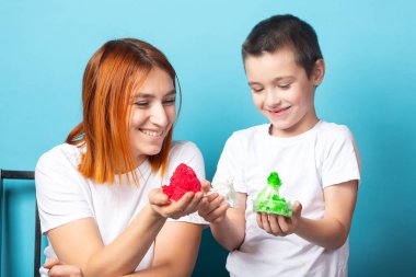 Anne ve oğlu büyüyen kırmızı ve yeşil kristalleri ellerinde tutuyorlar. Bu kristalleri mavi arka plandaki kimyasal bir deney sonucunda kendileri yaptılar. Büyüyen kristaller üzerinde kimyasal bir deney.