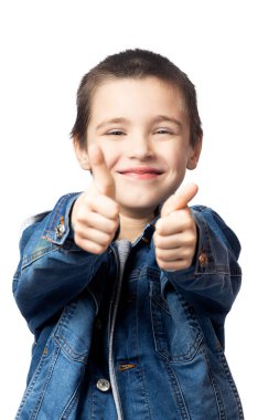 Kot ceketli, mutlu gülümseyen bir çocuğun portresi başparmaklarını kaldırıyor ve beyaz izole edilmiş arka planda eğleniyor.