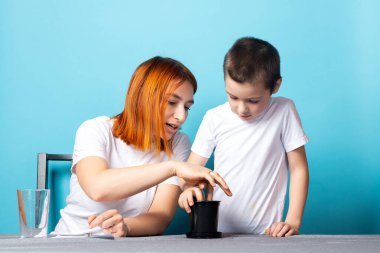 Anne ve oğlu, tohum ekmek ve mavi arka planda bir ev bitkisi yetiştirmek için siyah bir tencereye toprak koydular. Çocuklarla bahçe kursu kavramı.