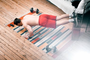 Genç adam spor için eve gider. Siyah saçlı sporcu şınav çeker ve yatak odasındaki halının üstünde egzersiz yapar.